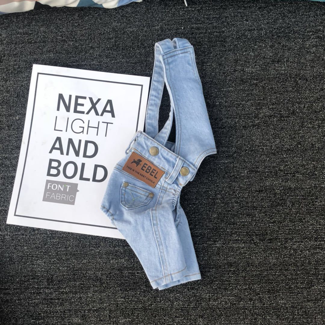 Light blue denim overalls with a brand label on a dark textured surface next to a sign with text.