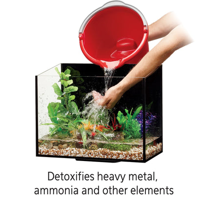 Person pouring water from a red bucket into an aquarium with plants and gravel.
