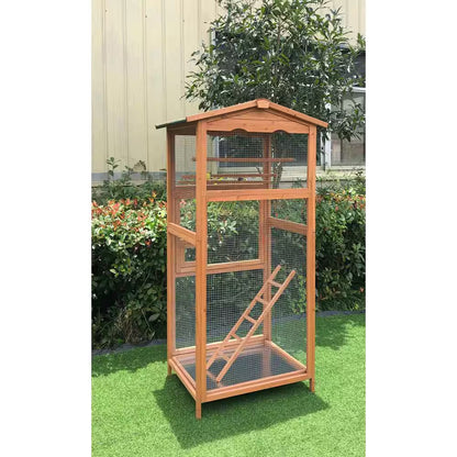 Wooden bird cage with a ramp on a grassy area with plants in the background