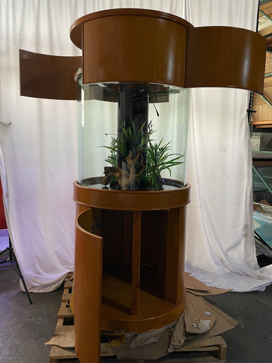Brown cylindrical plant stand with plants inside, on a pallet against a white curtain background.
