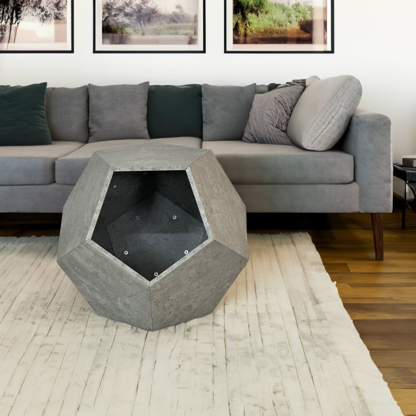 Hexagonal concrete table in a living room setting with a gray sectional sofa and framed pictures on the wall.