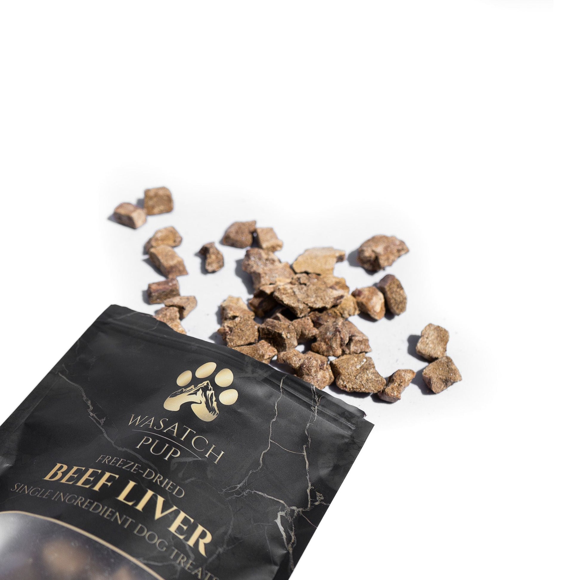 Wasatch Pup beef liver dog treats spilling out of a black packaging on a white background