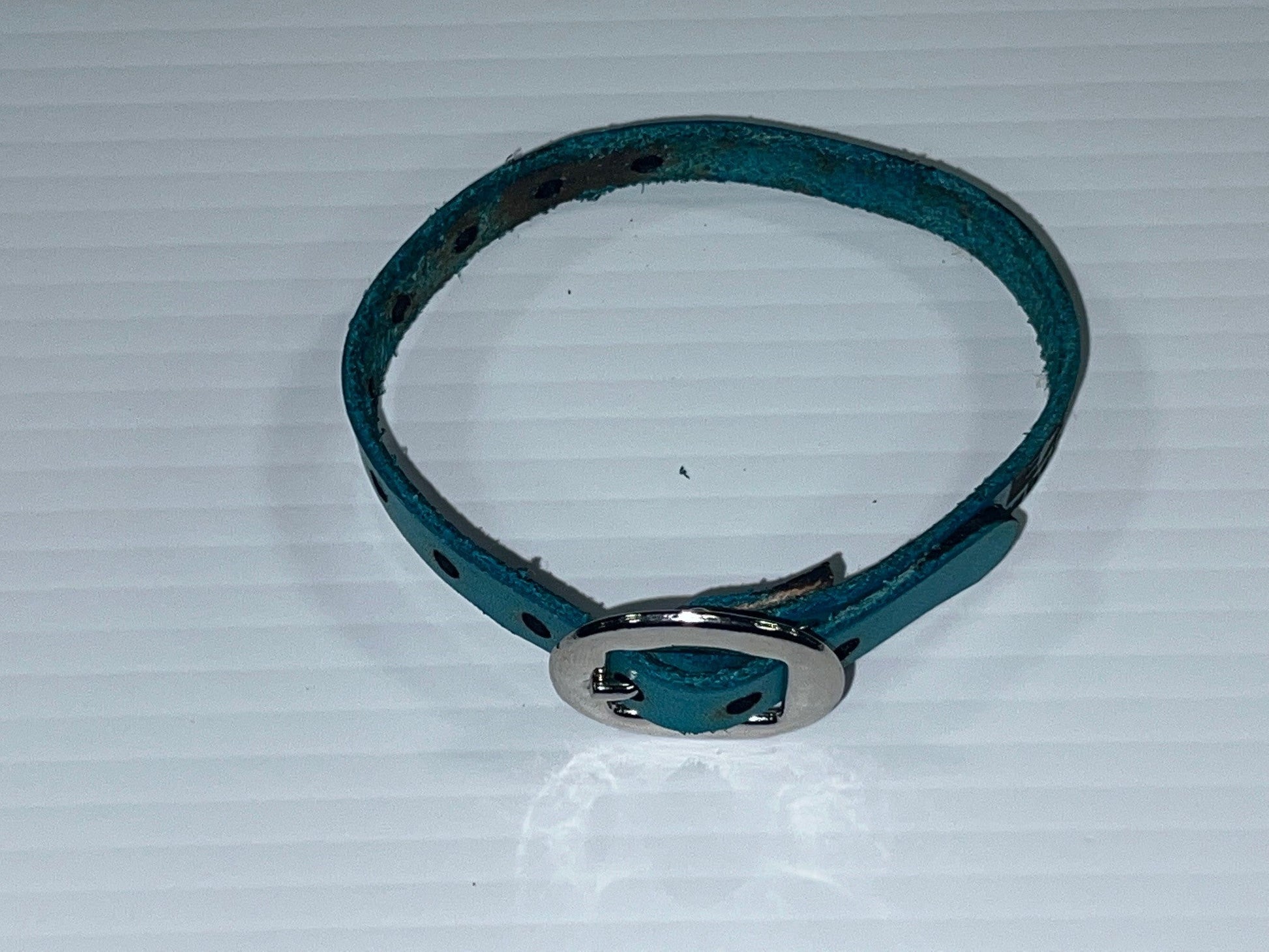 Teal leather bracelet with silver buckle on a white background