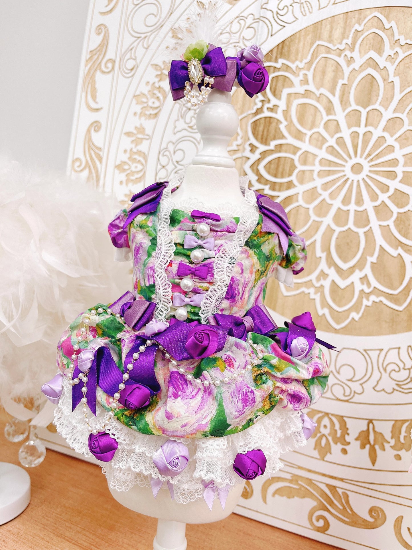 Decorative cake with purple and pink flowers on a white stand against an ornate white background.