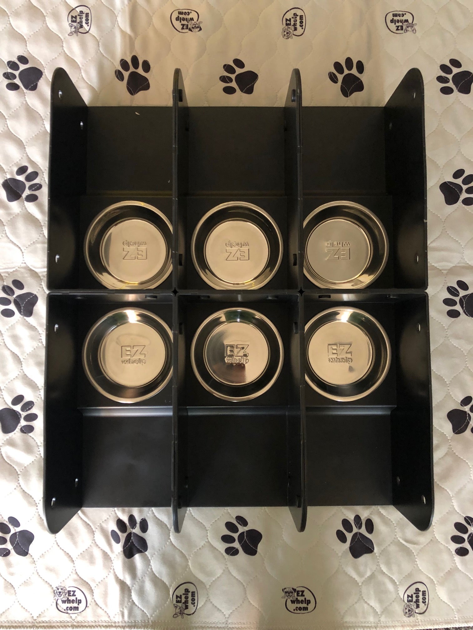 Black pet feeding station with six round gold-colored bowls on a patterned background.
