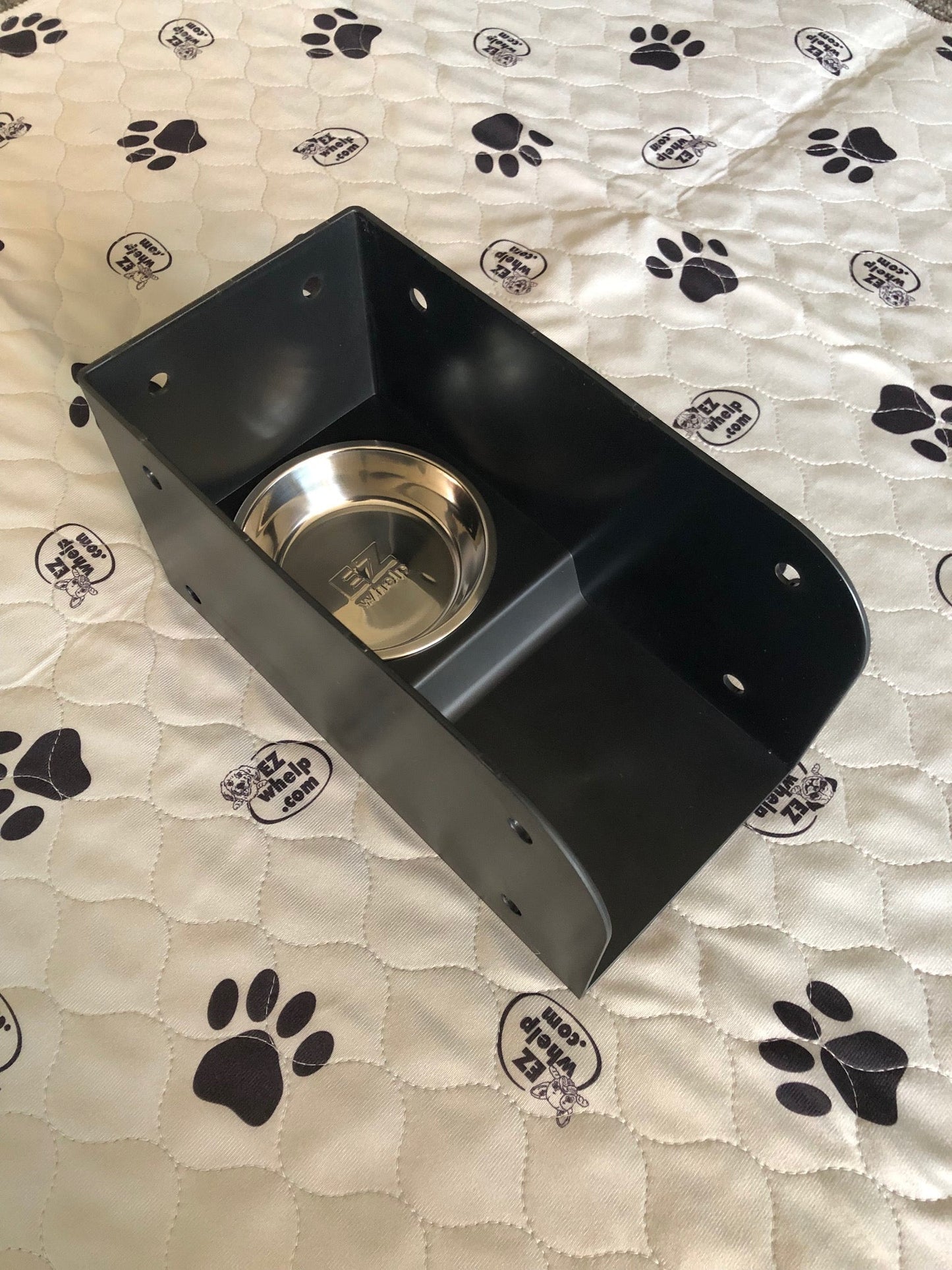 Black pet feeder with a metal bowl on a blanket with paw prints
