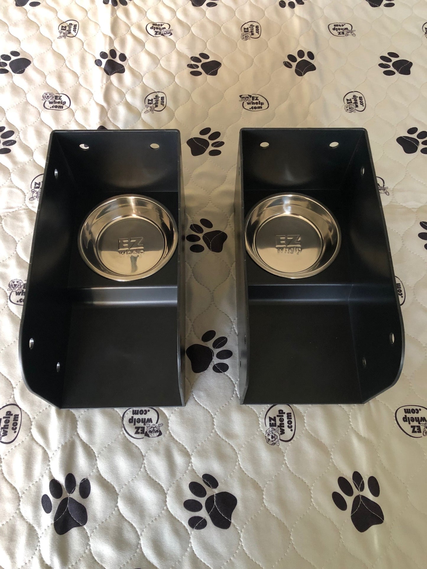 Two black pet bowls with silver bases on a white surface with black paw prints.