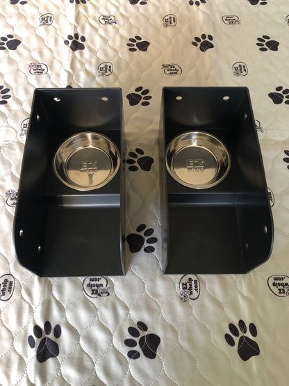 Two black pet bowls with silver bases on a white surface with black paw prints.
