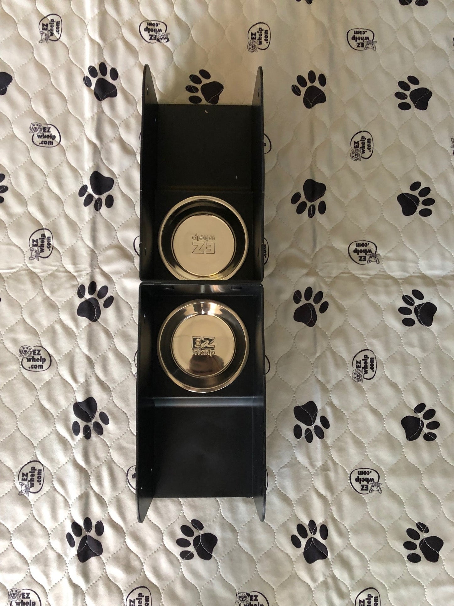 Two gold circular items in a black box on a white surface with black paw prints.