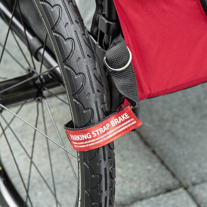Bicycle wheel with a red 'Parking Strap Brake' label on a pavement background