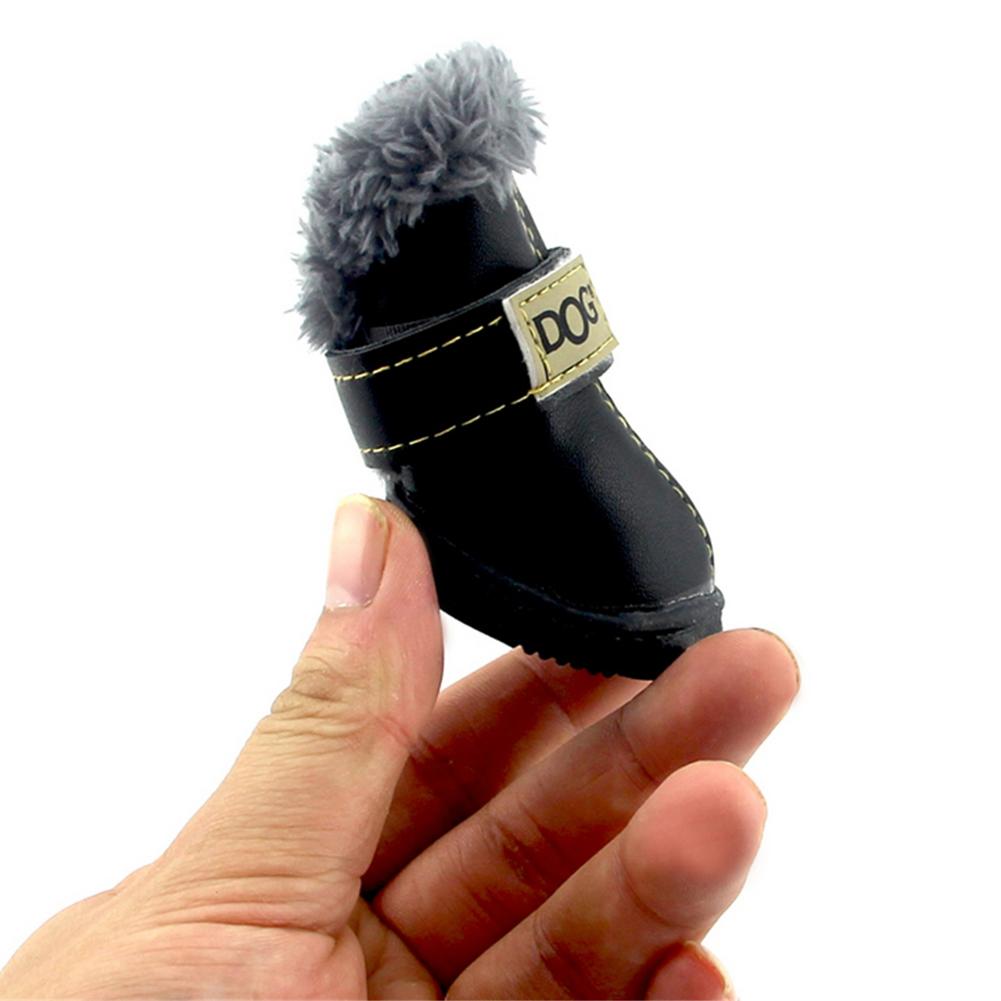 Black dog boot with gray fur on top held in a hand against a white background