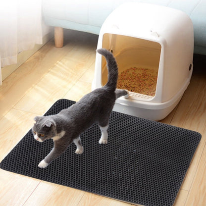 Cat stepping onto a black litter mat next to a white litter box on a wooden floor.