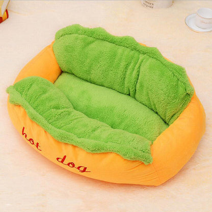 Dog bed shaped like a hot dog with green plush padding on a light background