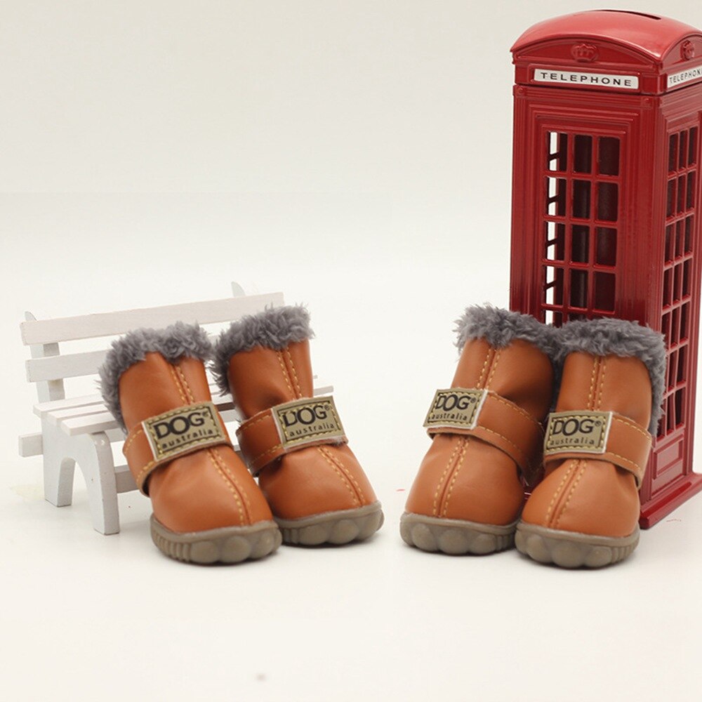 Pair of brown dog boots with gray fur lining in front of a red telephone box and white bench.