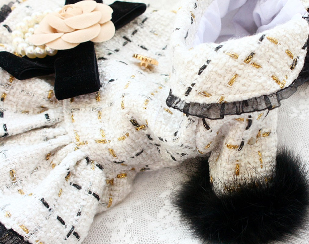 White textured fabric with black and gold patterns and a fluffy black pom-pom.