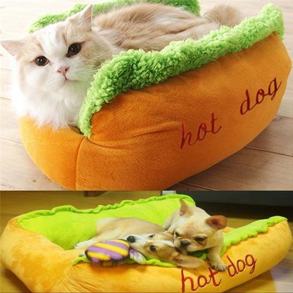 Cat and dog lying on a hot dog-shaped pet bed with green lettuce and orange bun.