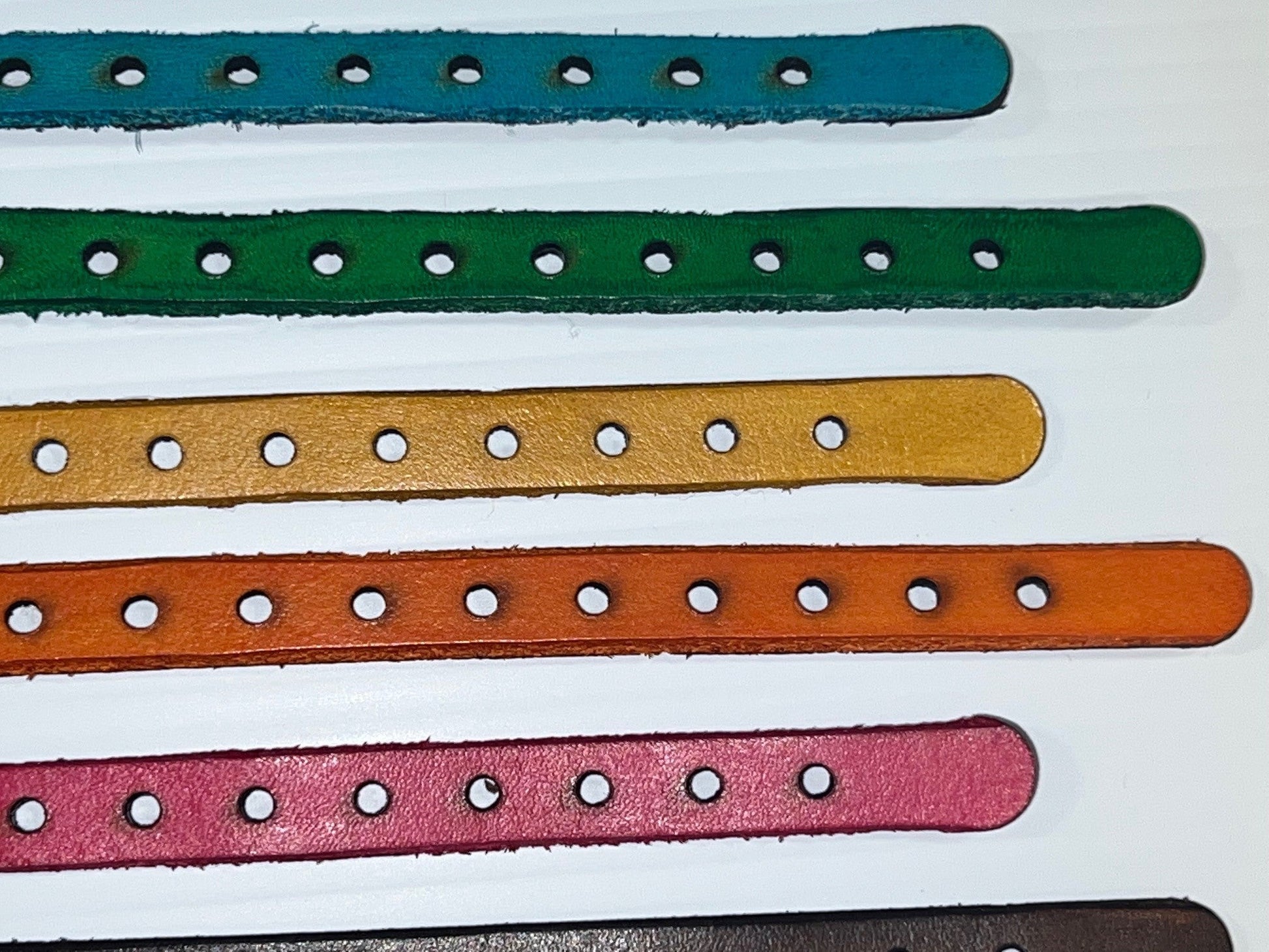 Five colorful leather straps with holes on a white background