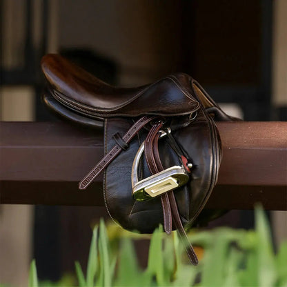 Brown leather saddle on a wooden fence with blurred background