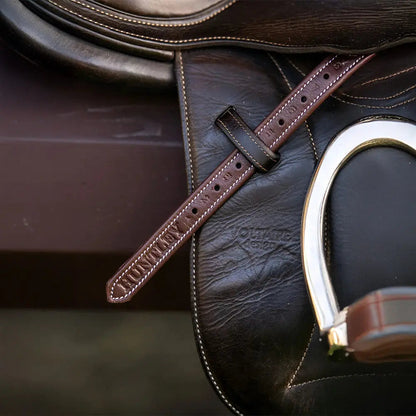 Brown leather saddle with a metal stirrup on a dark background