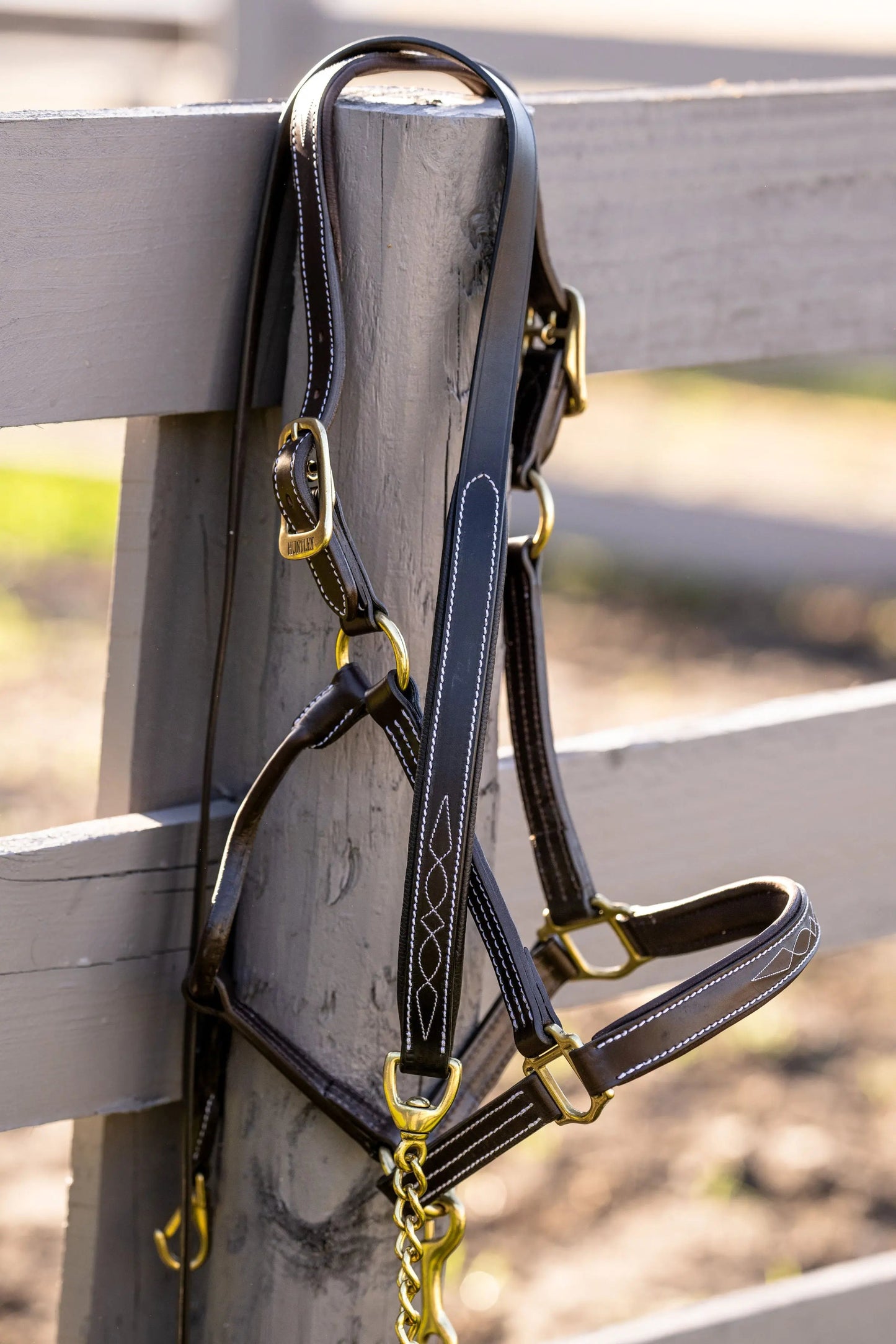 Black leather bridle with gold hardware on a wooden fence