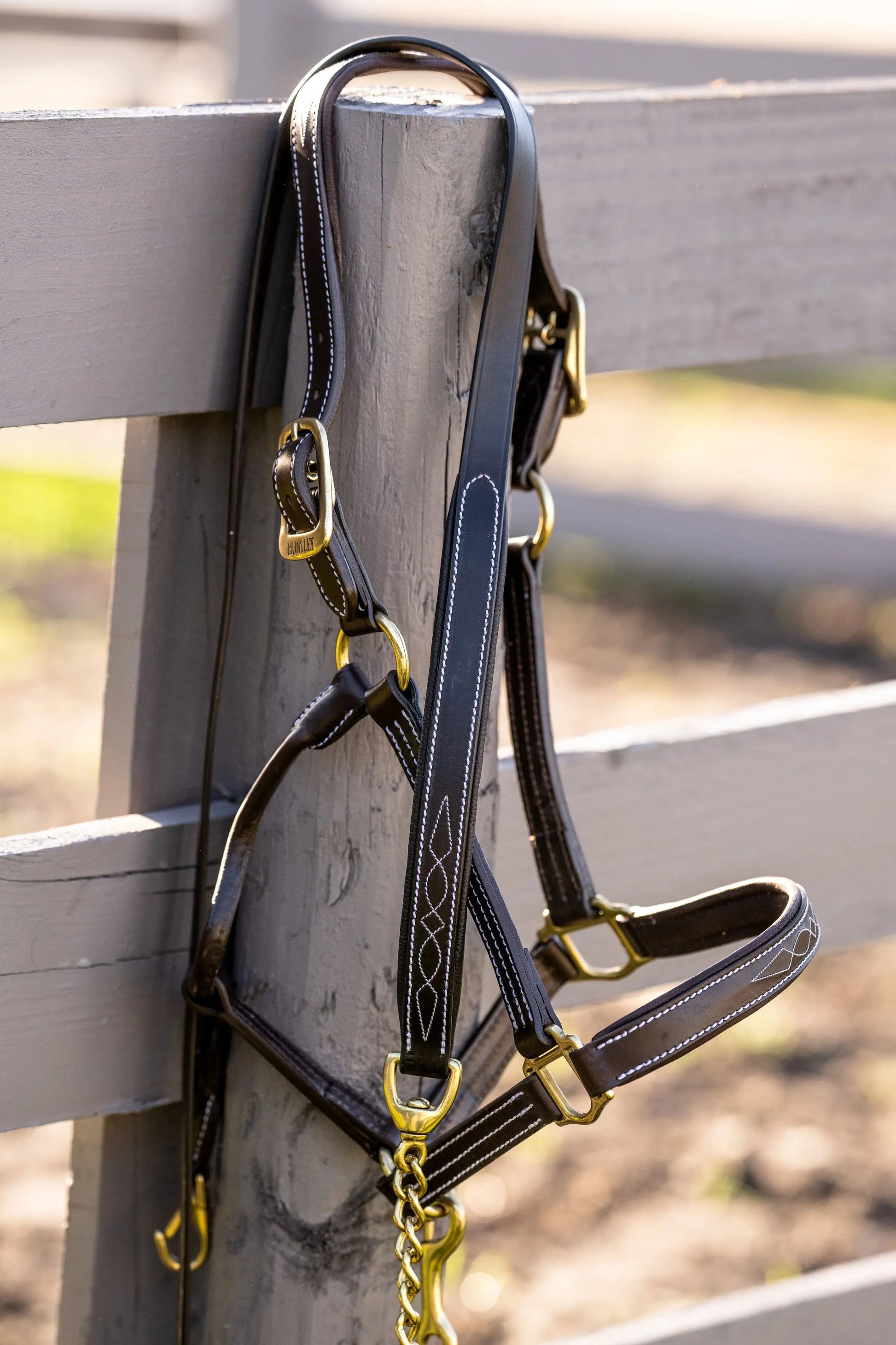 Black leather bridle with gold hardware on a wooden fence