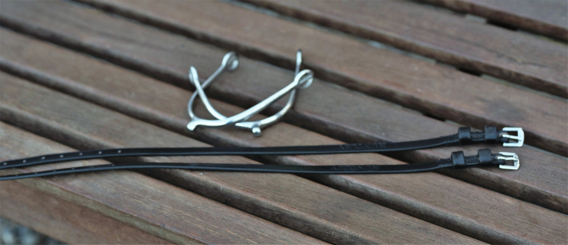 Two black straps with metal buckles on a wooden surface