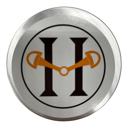Circular metal badge with a logo featuring a stylized 'H' with orange accents on a white background