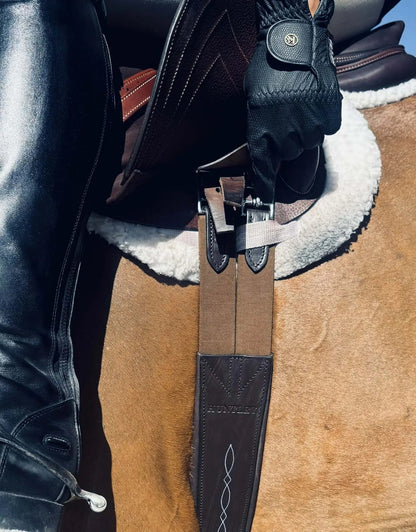 Close-up of a gloved hand adjusting a saddle on a horse, with a boot visible.