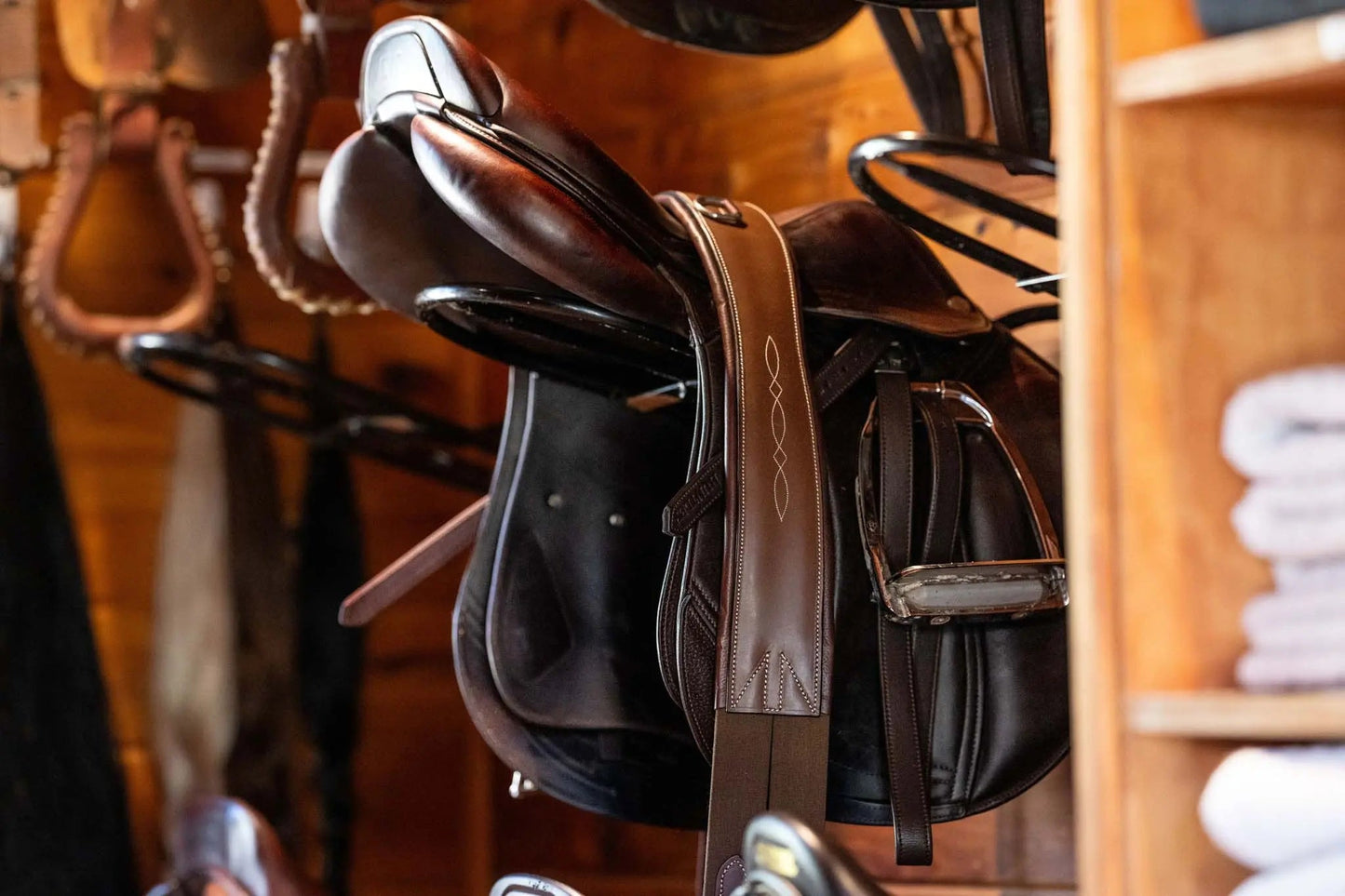 Brown leather saddle on a wooden rack with a blurred background