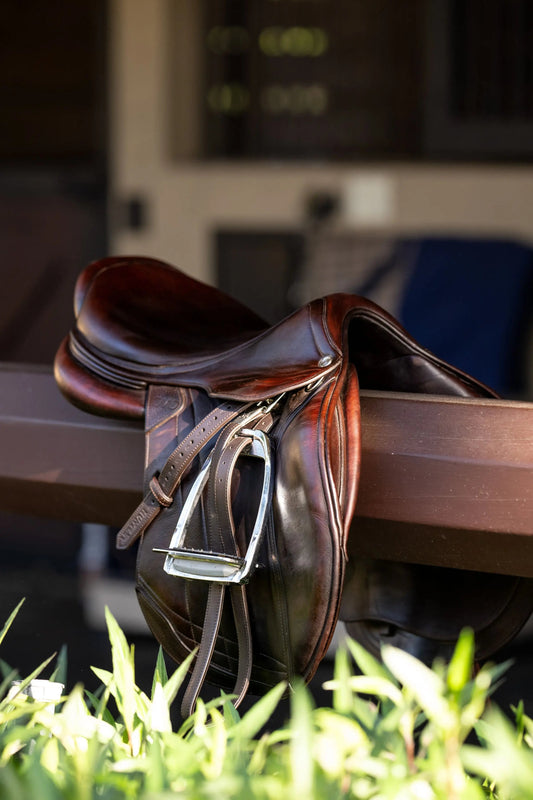 Brown leather saddle on a wooden stand with grass in the foreground