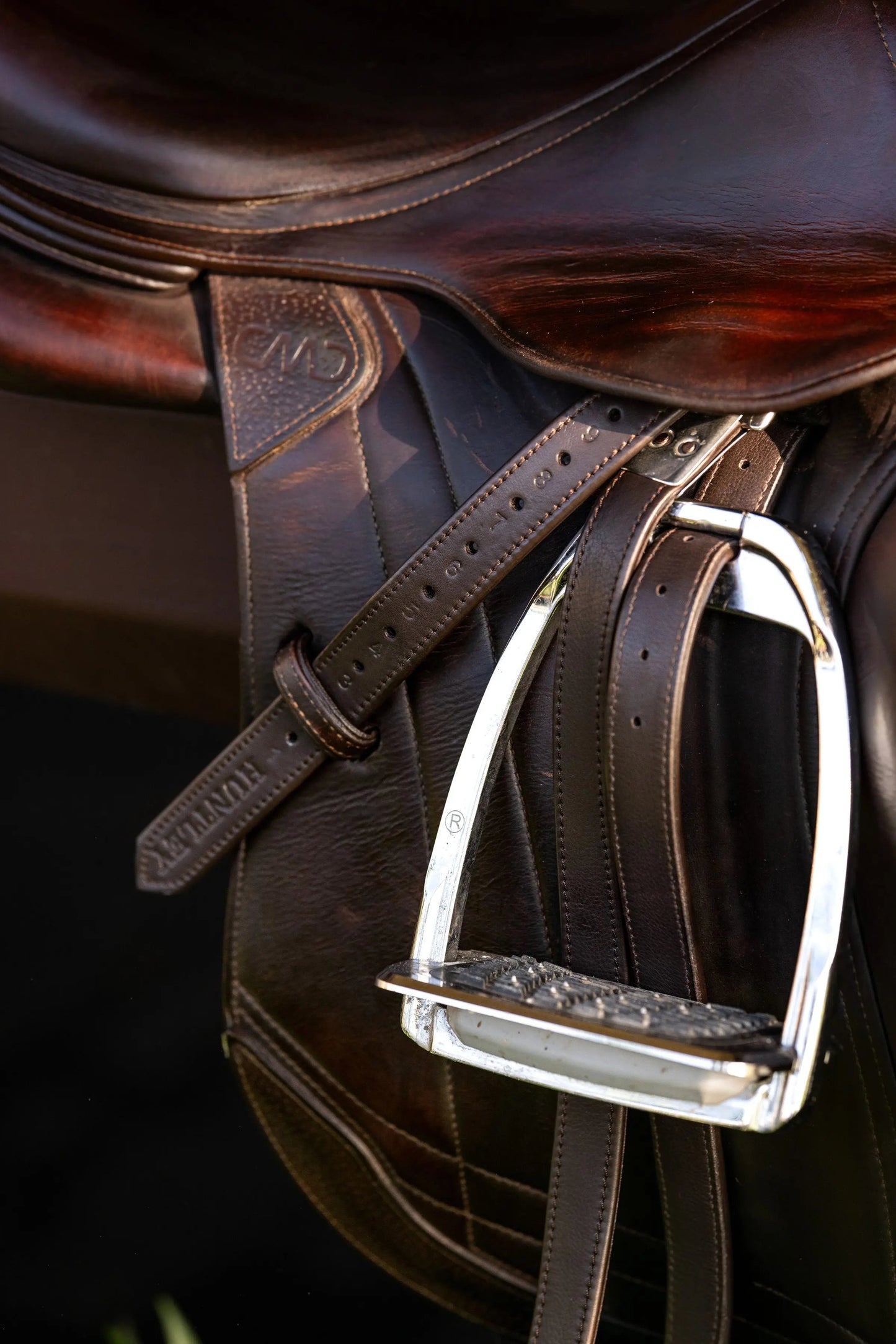 Close-up of a brown leather saddle with a metal stirrup on a dark background