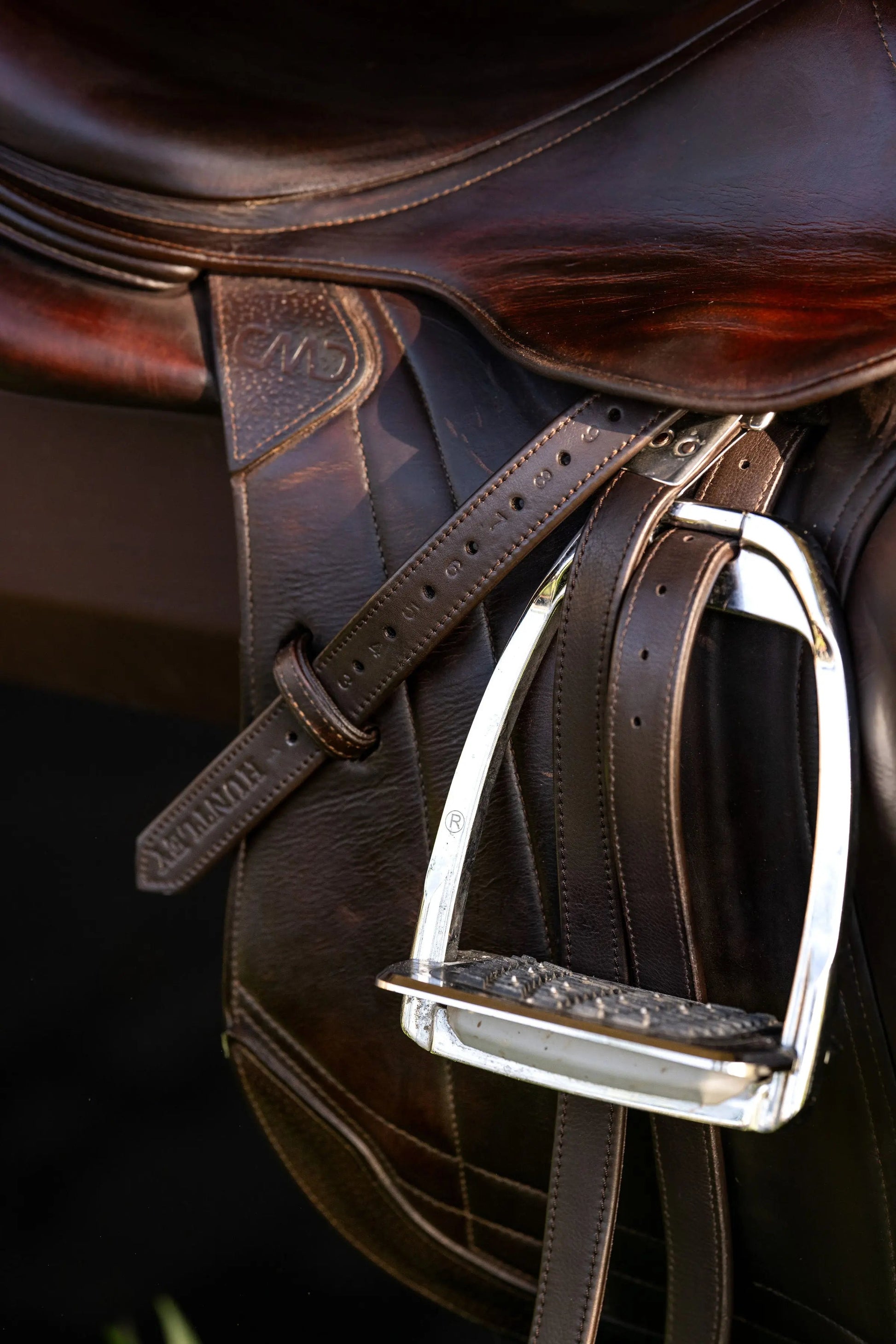 Close-up of a brown leather saddle with a metal stirrup on a dark background