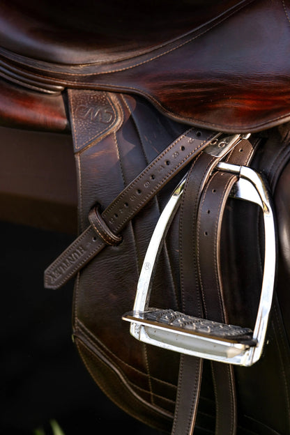 Close-up of a brown leather saddle with a metal stirrup on a dark background