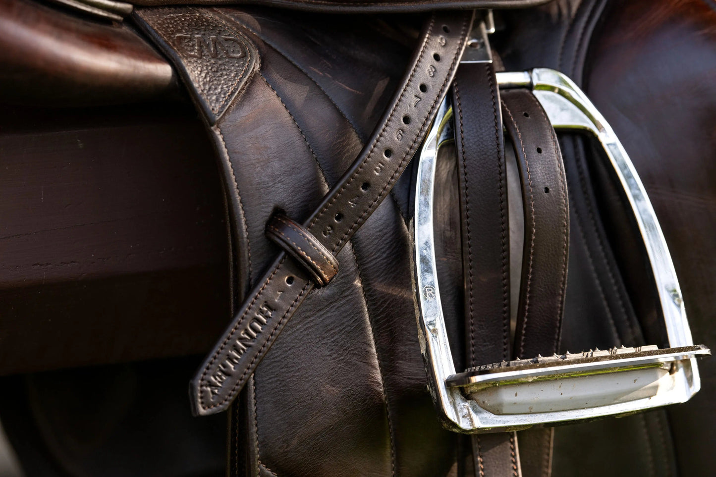 Close-up of a brown leather saddle with a metal stirrup on a horse.