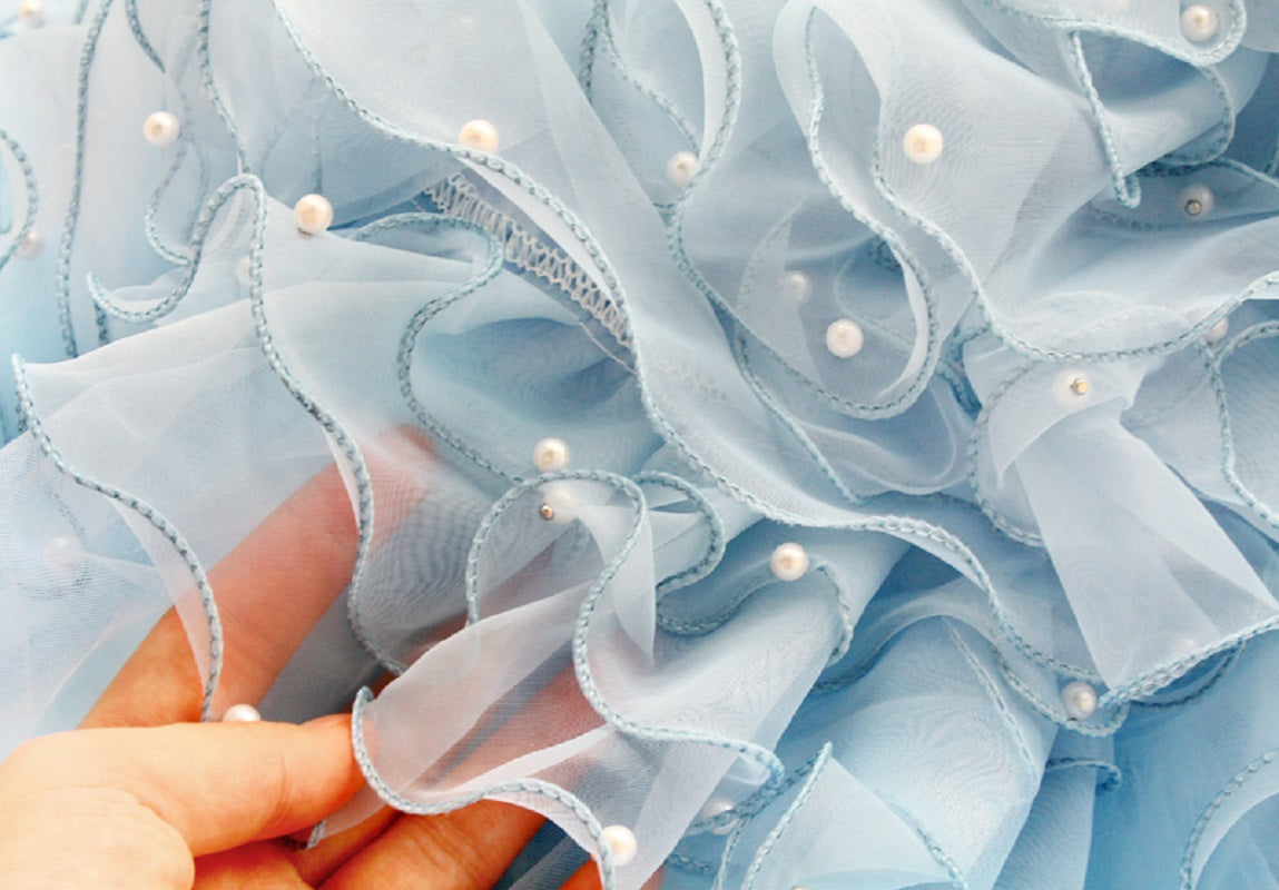 Close-up of light blue ruffled fabric with pearls held by a hand.