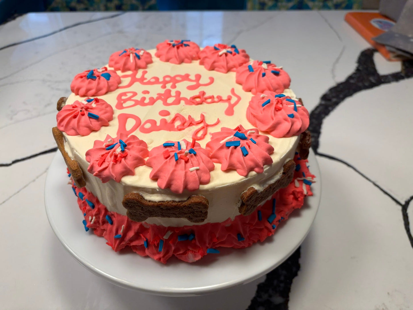 Birthday cake with pink frosting and 'Happy Birthday Daisy' text on a white plate.