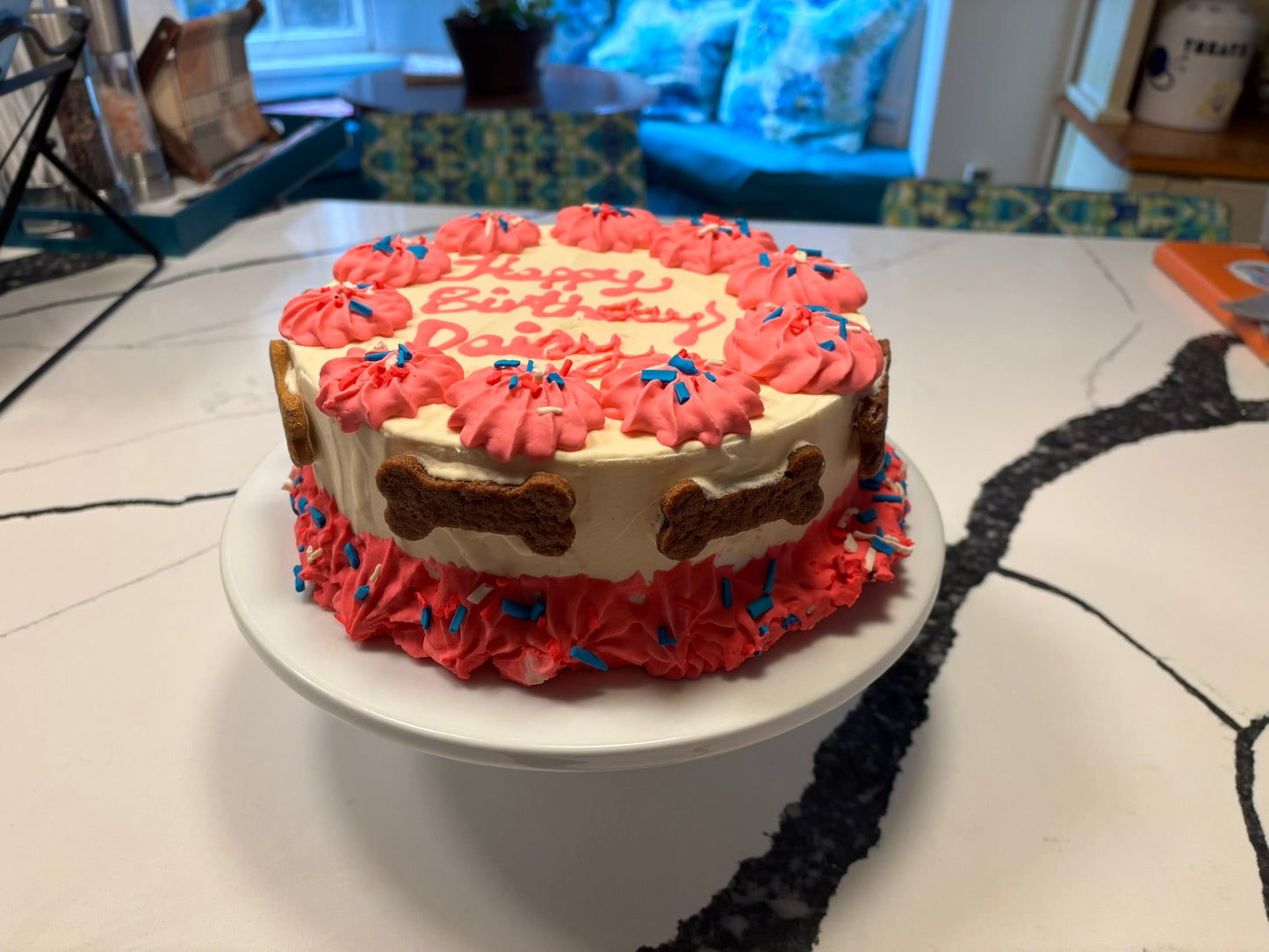Dog birthday cake with red frosting and bone decorations on a white plate.
