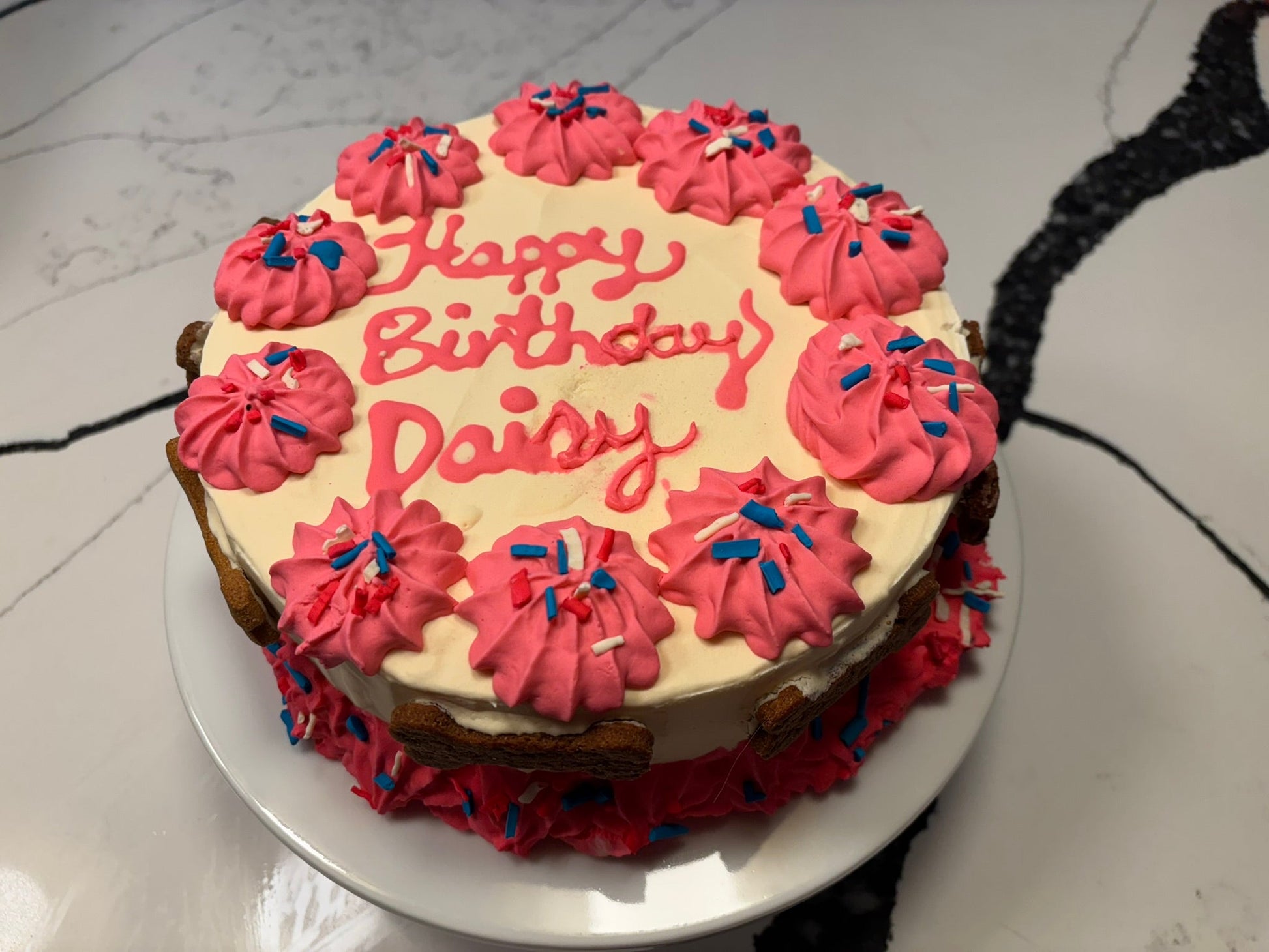 Birthday cake with pink frosting and 'Happy Birthday Daisy' text on a white plate.