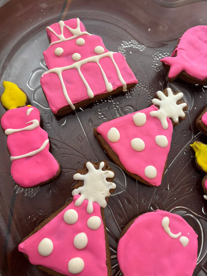 Decorative cookies shaped like a birthday cake, slice of pizza, and party hats on a dark surface.