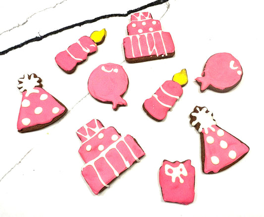 Decorative pink cookies shaped like birthday hats, balloons, and cakes on a white background.