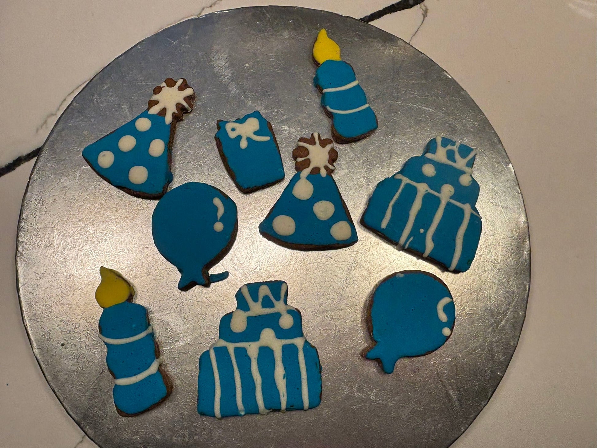 Decorative cookies shaped like birthday cakes, balloons, and candles on a metal tray.