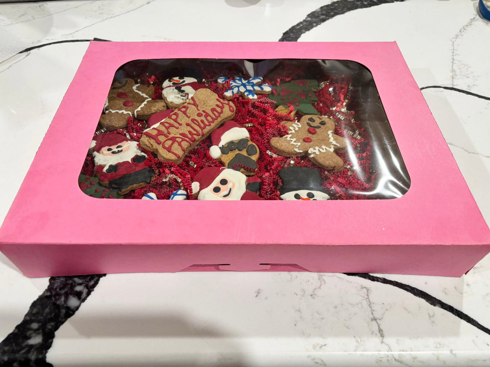 Pink gift box with Christmas-themed cookies inside on a marble surface