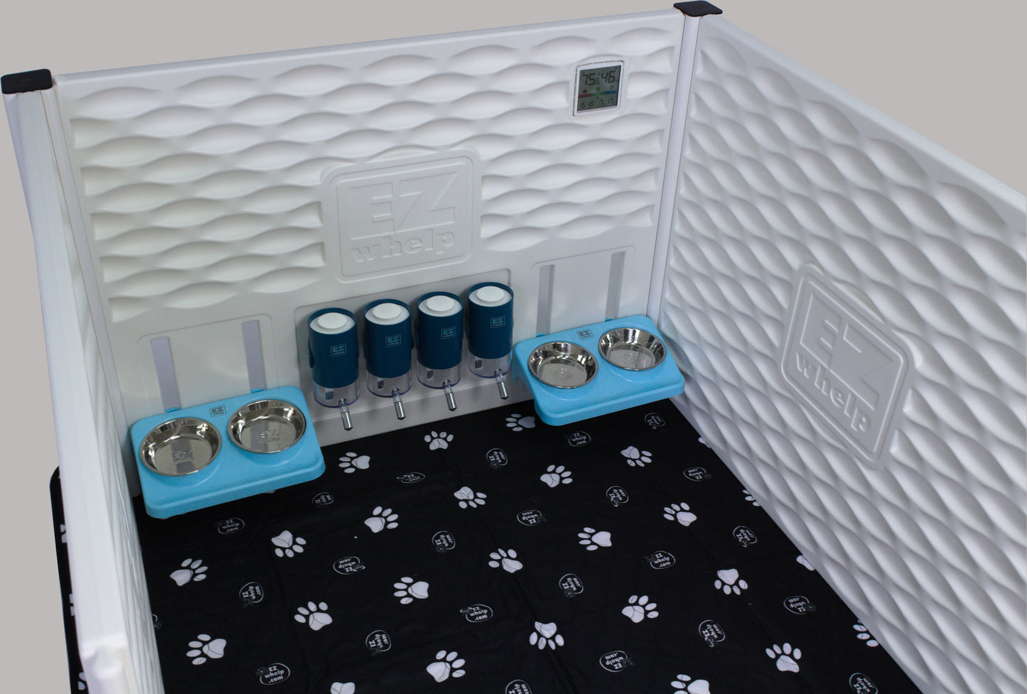 Pet crate with bedding, water bottles, and bowls on a black paw print mat.