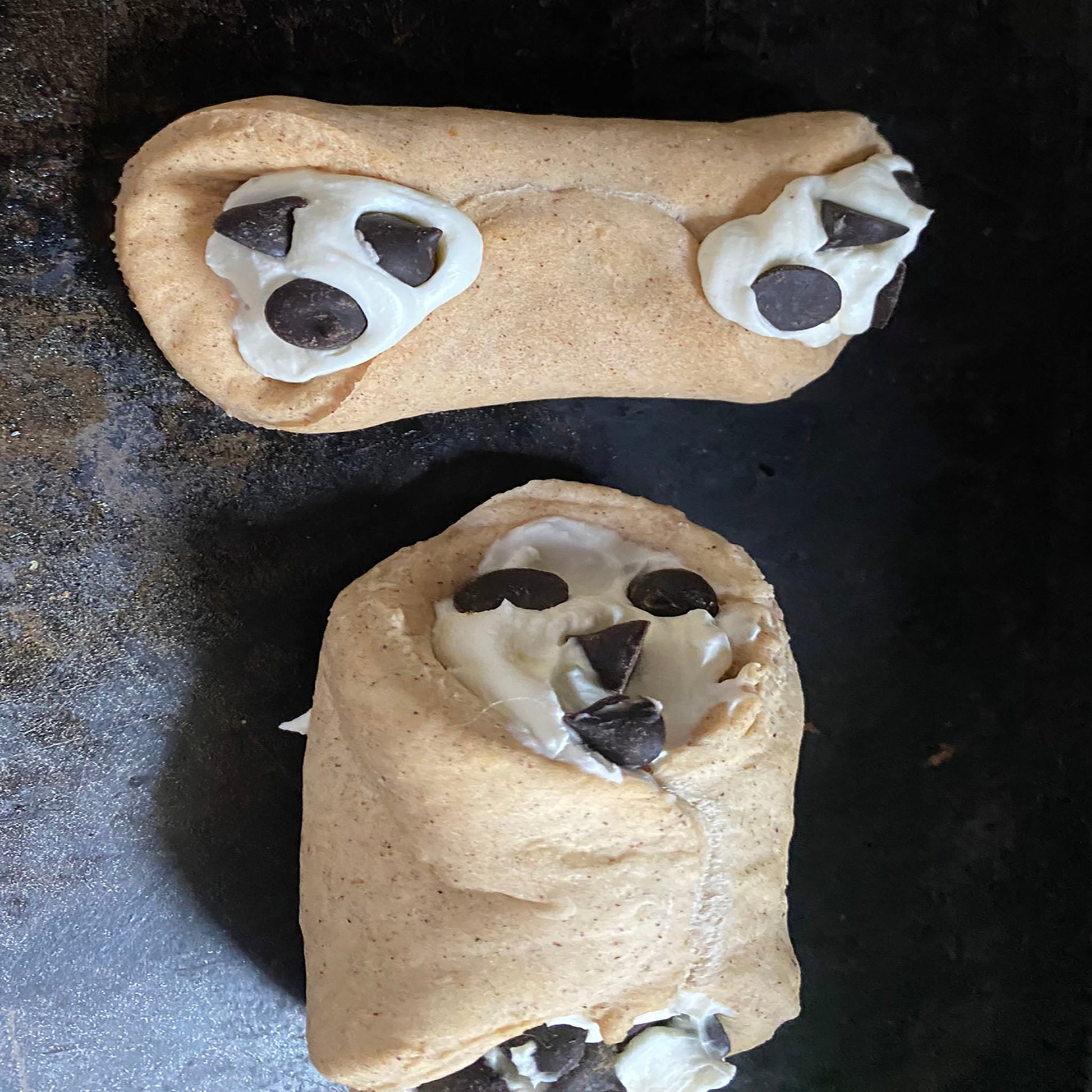 Two cookie-shaped treats with chocolate chips on a dark surface