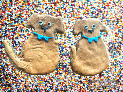 Two dog-shaped cookies with blue collars on a colorful sprinkles background