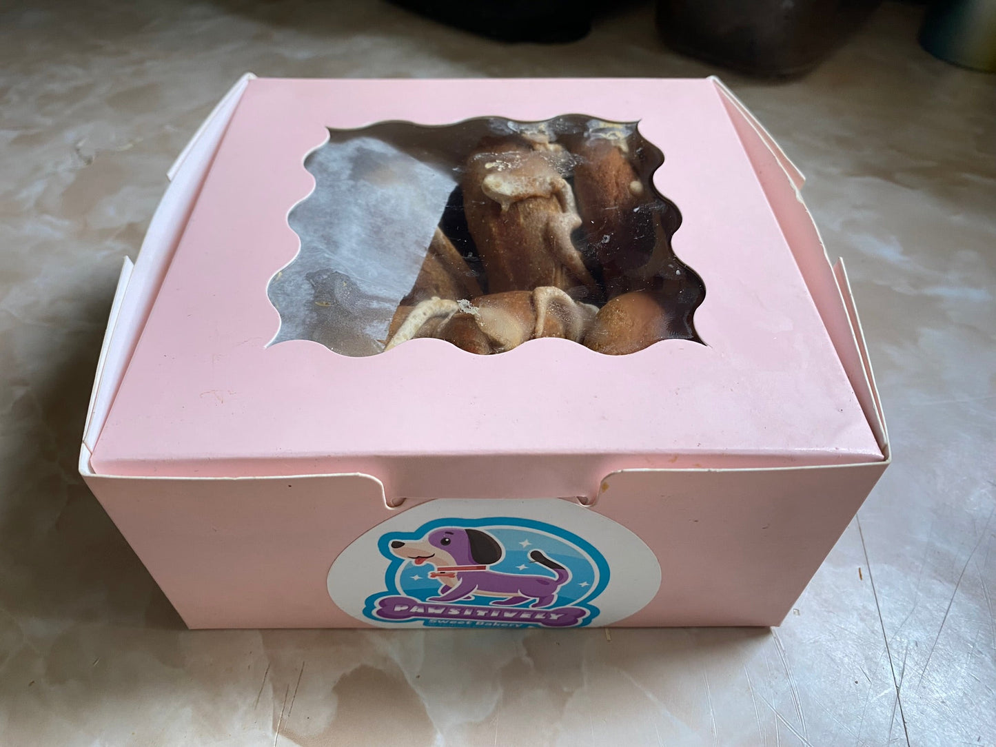 Pink box with a window displaying pastries on a marble surface