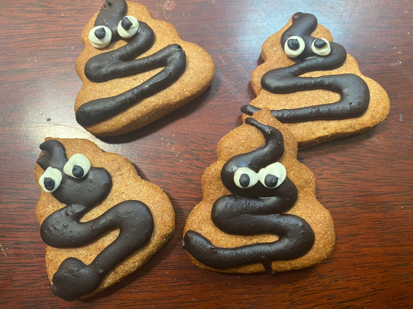 Three cookies shaped like poop with chocolate 'poop' and candy eyes on a wooden surface.