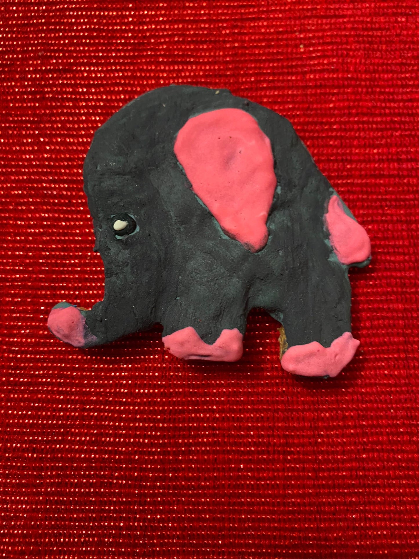 Plush elephant toy with pink ears on a red textured background
