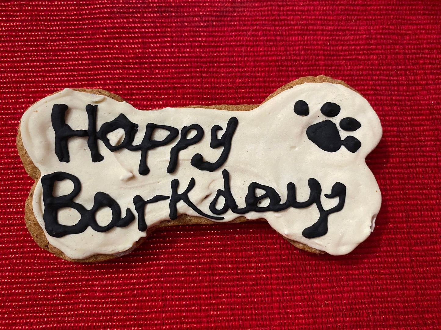 Dog bone-shaped cookie with 'Happy Barkday' text on a red background