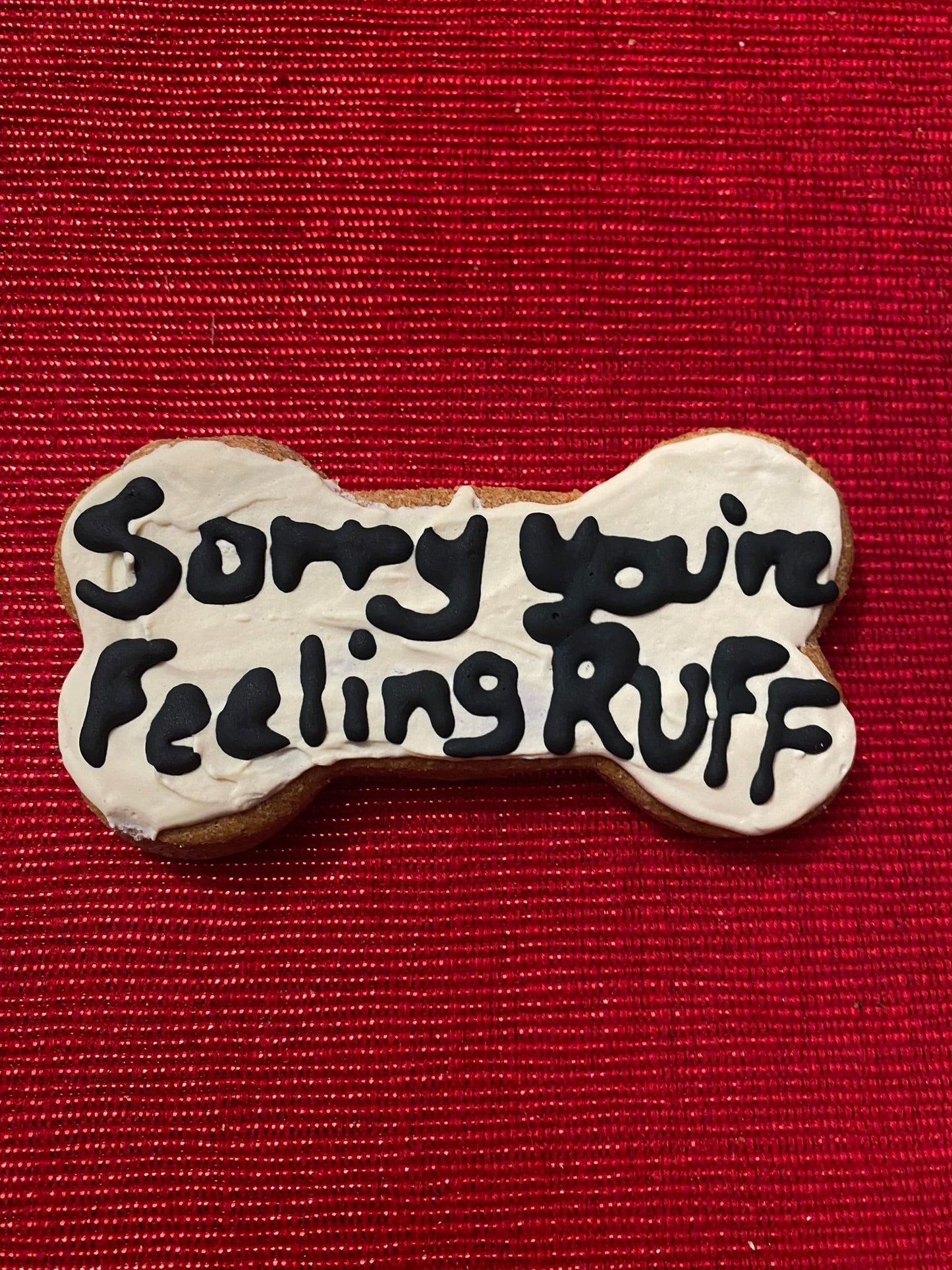 Dog bone-shaped cookie with 'Sorry your feeling ruff' text on a red background